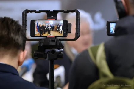 Uczestnicy konferencji prasowej na granicy w Barwinku na ekranie telefonu komórkowego.