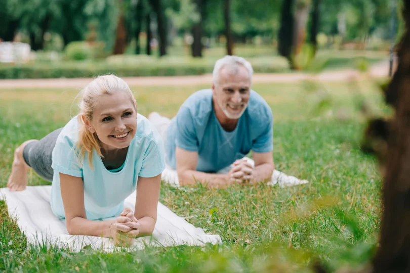 Zdjęcie przedstawiające dwoje uśmiechniętych seniorów - kobietę i mężczyznę leżących na trawie, podpartych na łokciach.