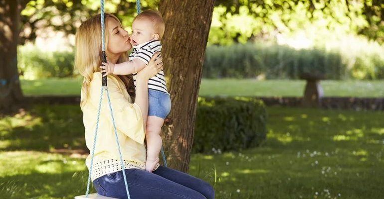 Grafika przedstawia kobietę (mamę) trzymająca na rękach malutkie dziecko.