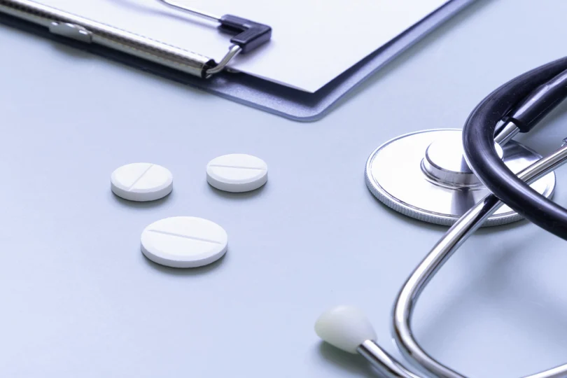 Grafika przedstawia leki, stetoskop i fragment bloczku z receptami