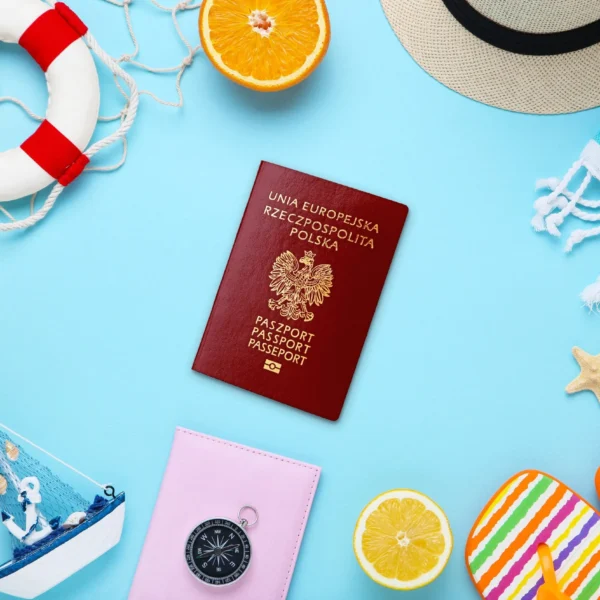 na niebieskim tle grafiki na środku widnieje paszport, a dookoła rzeczy kojarzące się z wakacjami: klapki plażowe, rozgwiazdy, ręcznik, kompas, koło ratunkowe, łódka, kapelusz, olejek do opalania i cząstki pomarańczy.